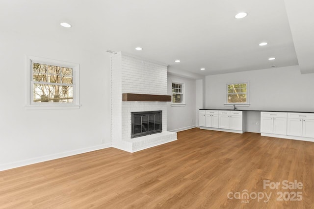 unfurnished living room featuring light wood-type flooring, recessed lighting, baseboards, a brick fireplace, and a sink