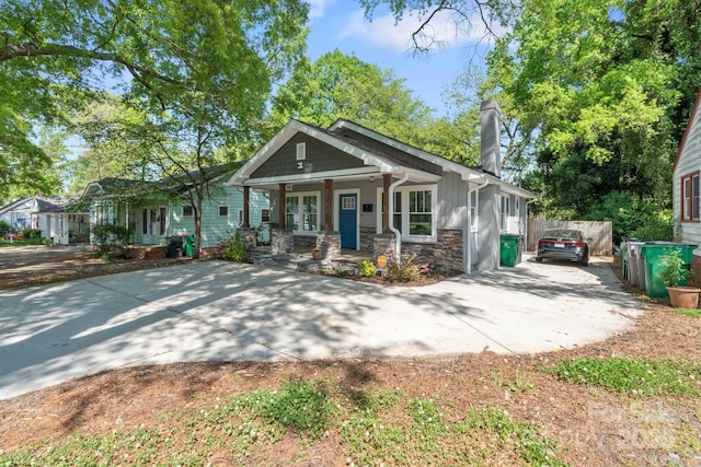 craftsman house featuring a chimney, driveway, stone siding, a porch, and fence
