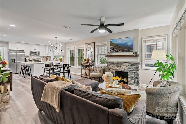 living area with visible vents, light wood-style floors, a fireplace, recessed lighting, and ceiling fan with notable chandelier