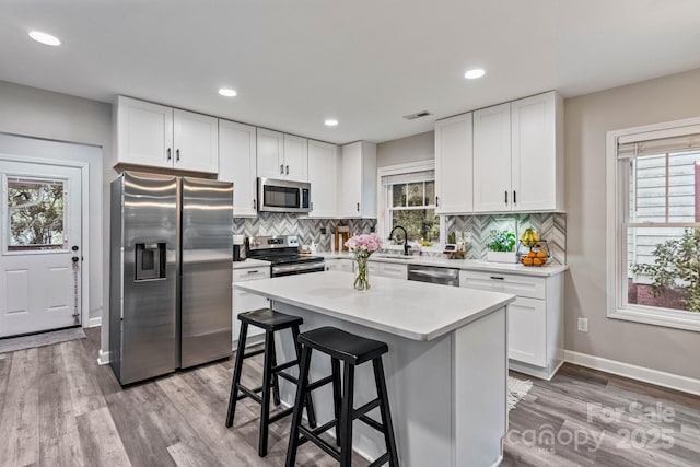 kitchen featuring visible vents, a sink, appliances with stainless steel finishes, wood finished floors, and backsplash