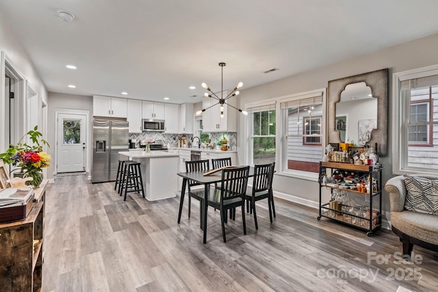 dining room with light wood-style flooring, recessed lighting, a notable chandelier, and a healthy amount of sunlight