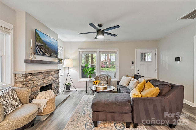 living room featuring ceiling fan, a fireplace, visible vents, wood finished floors, and baseboards