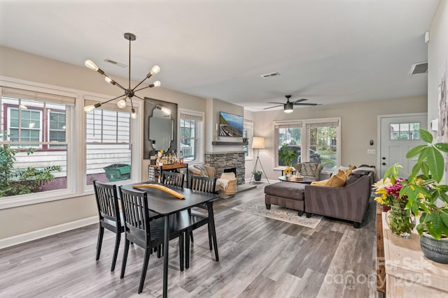 dining area with light wood-style floors, a fireplace, visible vents, and ceiling fan with notable chandelier