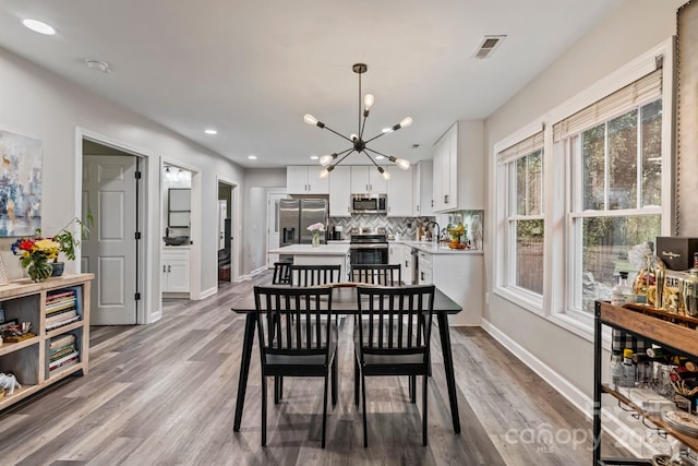 dining space with a chandelier, wood finished floors, baseboards, and visible vents