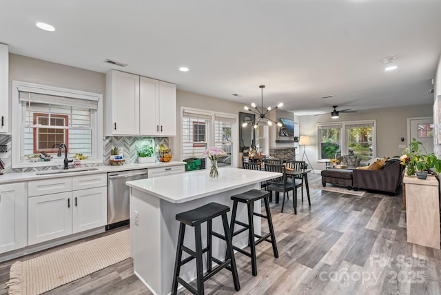 kitchen with stainless steel dishwasher, light wood-type flooring, white cabinetry, a sink, and decorative backsplash