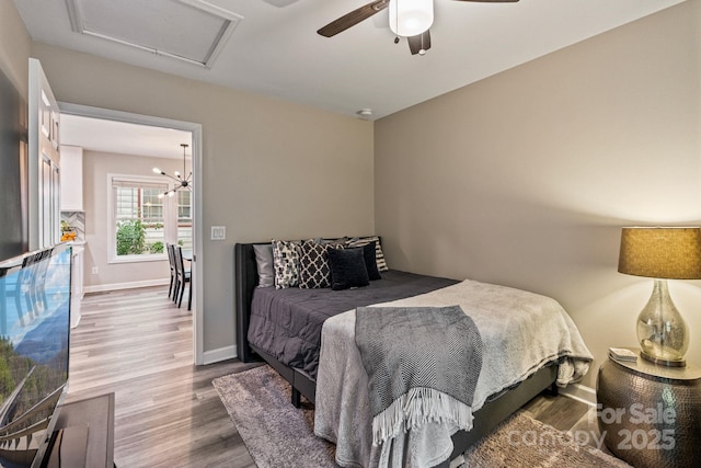 bedroom with baseboards, a ceiling fan, attic access, and wood finished floors