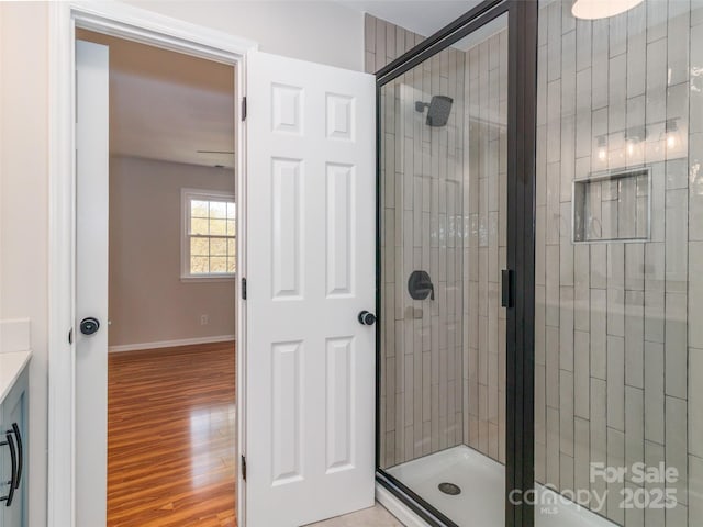 full bath featuring a stall shower, wood finished floors, and baseboards