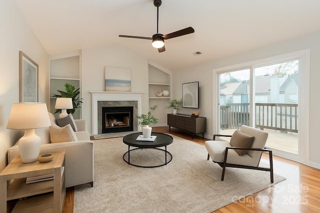 living area with built in features, a ceiling fan, visible vents, wood finished floors, and lofted ceiling