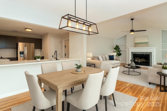 dining area with light wood-type flooring, ceiling fan, a glass covered fireplace, and vaulted ceiling