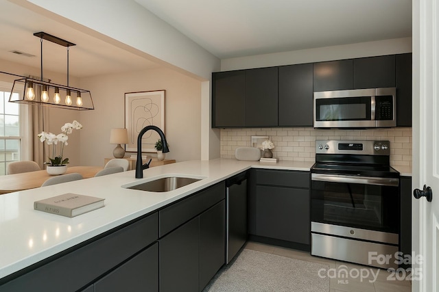 kitchen with tasteful backsplash, a sink, light countertops, appliances with stainless steel finishes, and pendant lighting