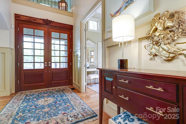 entryway with arched walkways, french doors, and light wood-style flooring