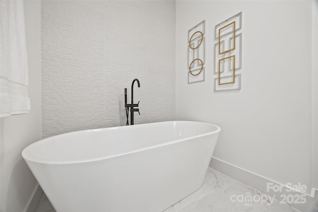 bathroom with marble finish floor, baseboards, and a soaking tub