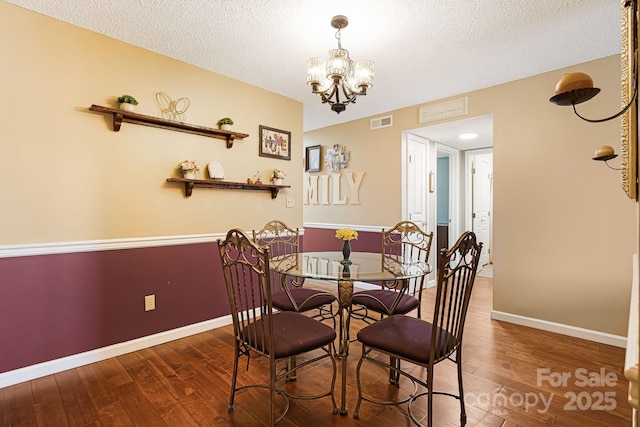 dining area with a textured ceiling, visible vents, an inviting chandelier, and hardwood / wood-style flooring