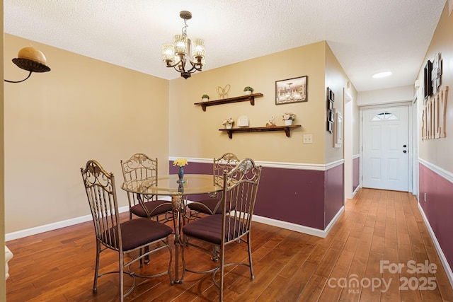 dining space featuring wood-type flooring, an inviting chandelier, baseboards, and a textured ceiling