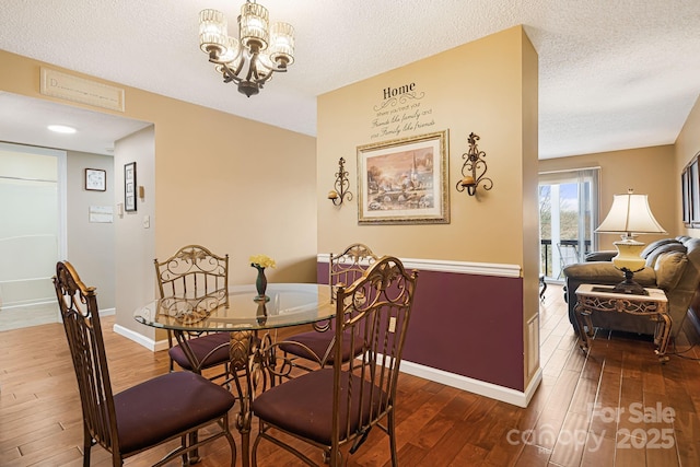 dining area with baseboards, a textured ceiling, a chandelier, and hardwood / wood-style flooring