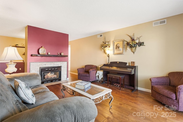 living area with baseboards, a fireplace, visible vents, and wood-type flooring