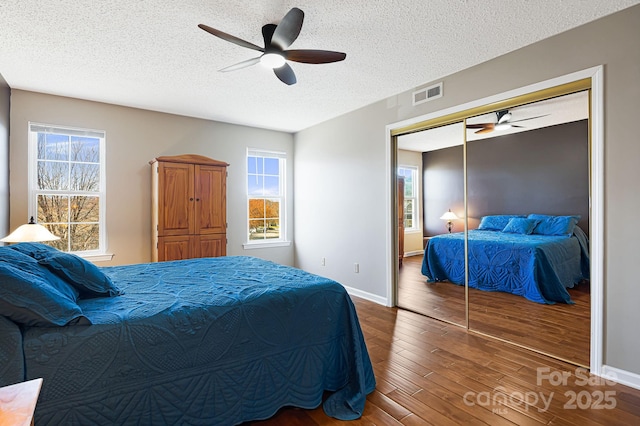bedroom with baseboards, a textured ceiling, ceiling fan, visible vents, and wood finished floors