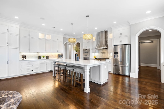 1311 Sunnys Halo Ln, Waxhaw, NC 28173 - kitchen featuring stainless steel appliances, arched walkways, wall chimney range hood, ornamental molding, and light countertops