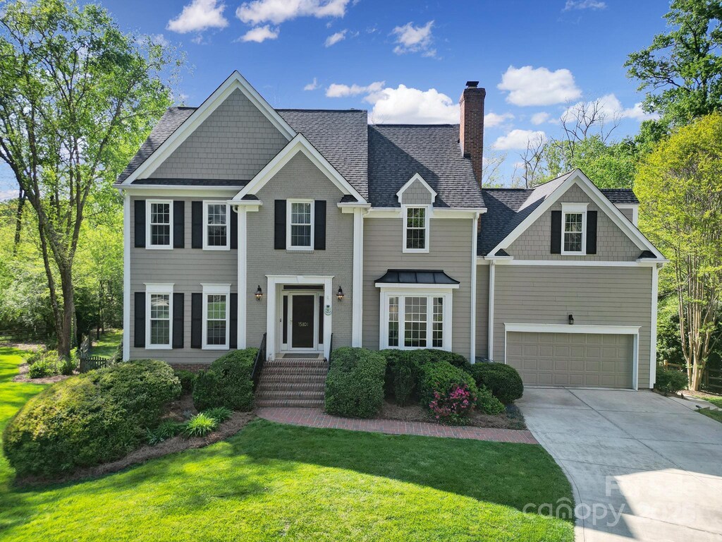 view of front facade featuring a front lawn, driveway, a chimney, an attached garage, and a shingled roof