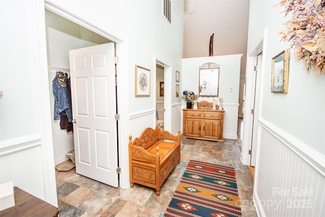 corridor with wainscoting, stone finish floors, a decorative wall, and a towering ceiling
