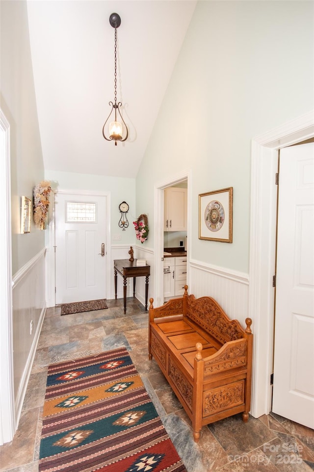 entrance foyer with high vaulted ceiling, a wainscoted wall, and stone finish flooring