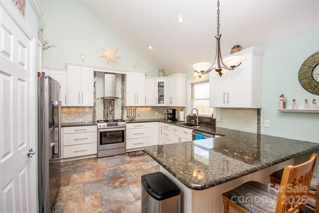 kitchen featuring stainless steel appliances, wall chimney exhaust hood, a peninsula, a sink, and decorative backsplash