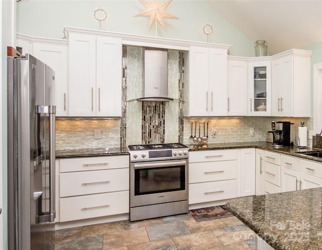 kitchen featuring appliances with stainless steel finishes, wall chimney range hood, white cabinetry, decorative backsplash, and glass insert cabinets