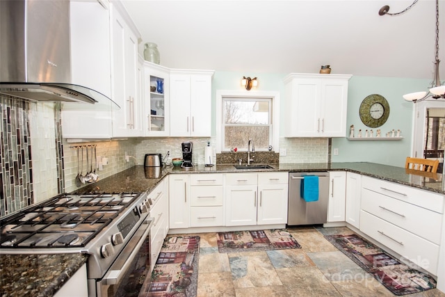 kitchen featuring wall chimney exhaust hood, appliances with stainless steel finishes, a sink, decorative backsplash, and white cabinetry