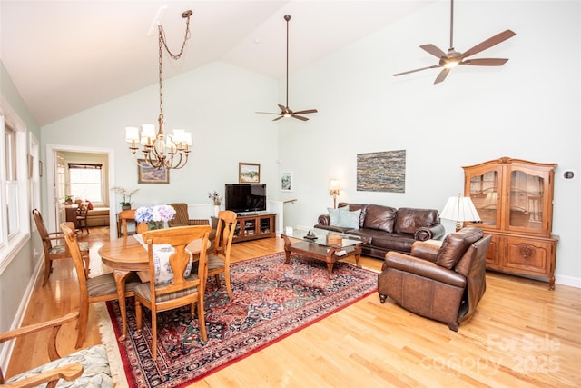 living area with ceiling fan, light wood-type flooring, high vaulted ceiling, a chandelier, and baseboards