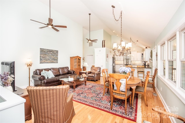 dining room featuring a ceiling fan, a chandelier, light wood-type flooring, high vaulted ceiling, and baseboards