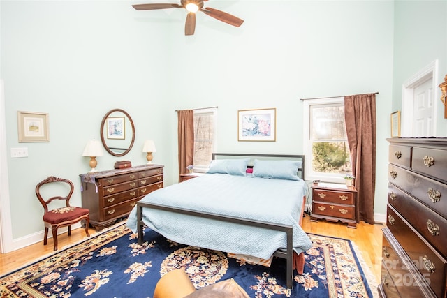 bedroom featuring a high ceiling, light wood-style floors, ceiling fan, and baseboards