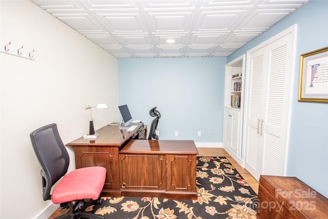 home office featuring wood finished floors, an ornate ceiling, and baseboards