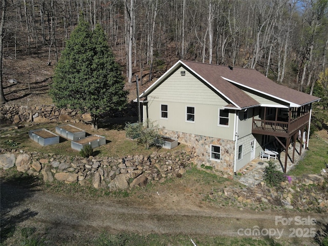 view of property exterior featuring a sunroom, stone siding, and a wooden deck