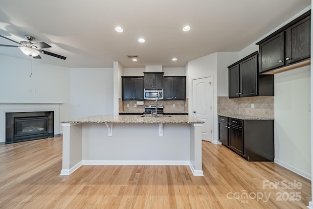 9001 Lanark Ln, Indian Land, SC 29707 - kitchen featuring appliances with stainless steel finishes, a glass covered fireplace, light wood-type flooring, tasteful backsplash, and light stone counters