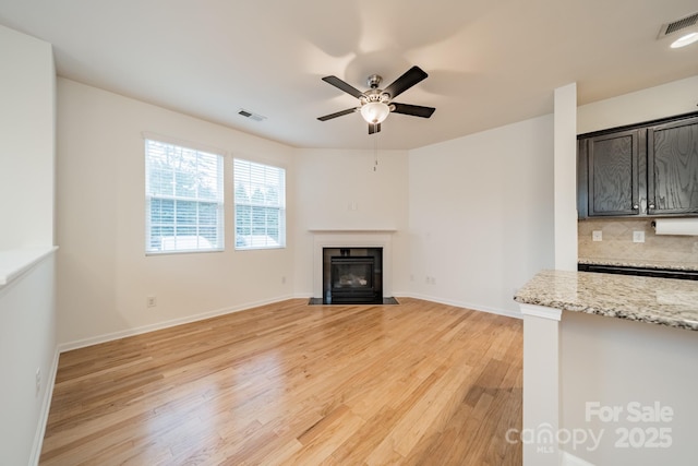 9001 Lanark Ln, Indian Land, SC 29707 - unfurnished living room with light wood-style floors, a ceiling fan, a fireplace with flush hearth, and baseboards