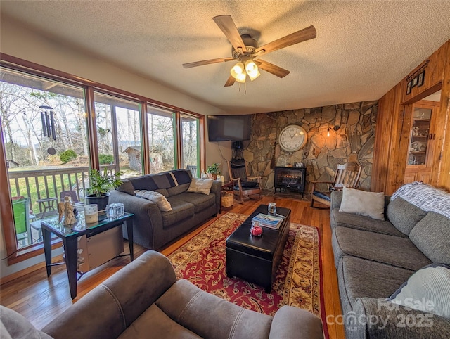 living room with wood-type flooring, a textured ceiling, a wood stove, and ceiling fan