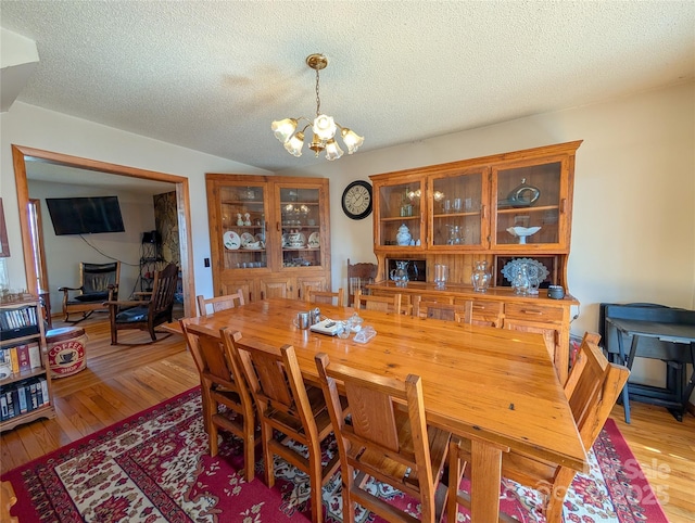 dining space with lofted ceiling, a textured ceiling, an inviting chandelier, and light wood finished floors