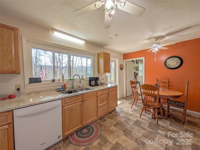 kitchen featuring light countertops, a sink, a ceiling fan, dishwasher, and stone finish floor