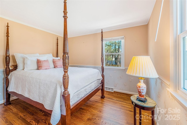 bedroom featuring wood finished floors, baseboards, ornamental molding, and visible vents