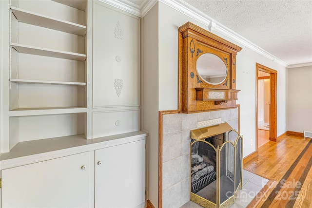 interior space with a textured ceiling, ornamental molding, visible vents, light wood finished floors, and heating unit