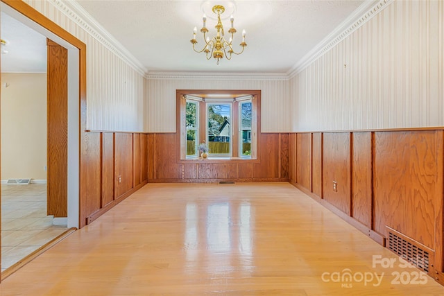 spare room with crown molding, visible vents, a chandelier, and wood finished floors