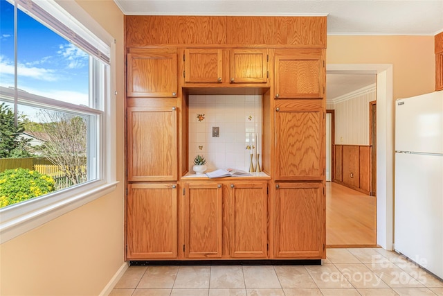 kitchen featuring light tile patterned floors, light countertops, freestanding refrigerator, crown molding, and brown cabinetry