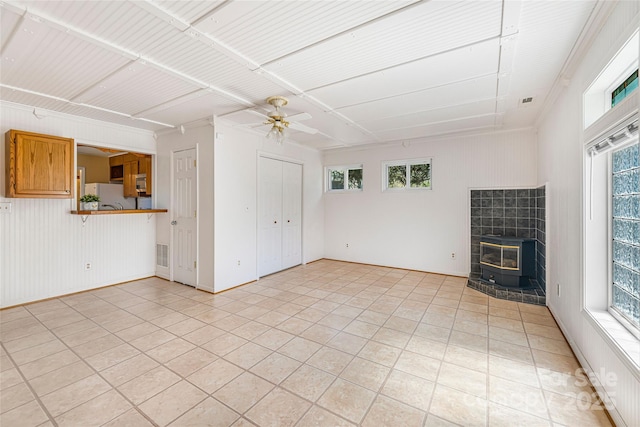 unfurnished living room featuring a wealth of natural light, a wood stove, visible vents, and ceiling fan