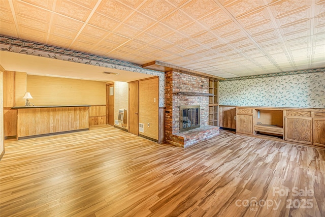 unfurnished living room featuring an ornate ceiling, a fireplace, wood finished floors, and wallpapered walls