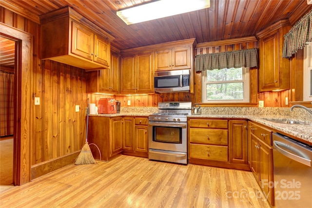 235 John Rainey Rd, Salisbury, NC 28147 - kitchen featuring appliances with stainless steel finishes, a sink, brown cabinets, light wood finished floors, and wood walls