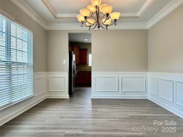 unfurnished dining area with crown molding, light wood finished floors, a wainscoted wall, and a notable chandelier