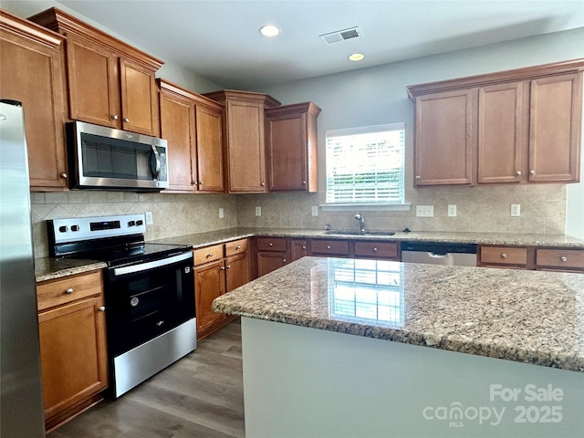 kitchen with light stone counters, appliances with stainless steel finishes, a sink, dark wood-type flooring, and visible vents