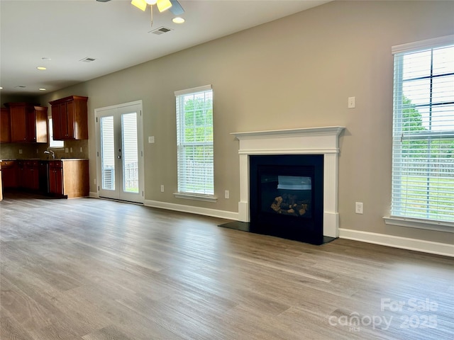 unfurnished living room with a ceiling fan, visible vents, baseboards, a glass covered fireplace, and light wood-style floors