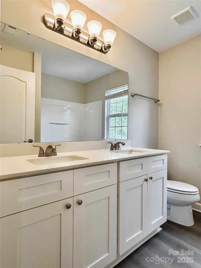 bathroom featuring double vanity, visible vents, wood finished floors, a sink, and toilet