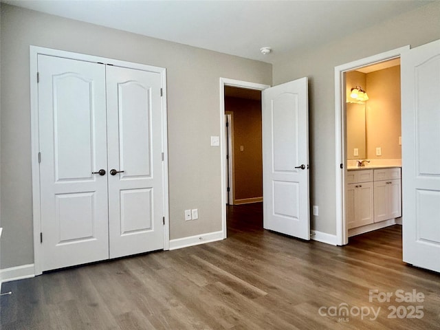 unfurnished bedroom featuring a sink, baseboards, a closet, and wood finished floors